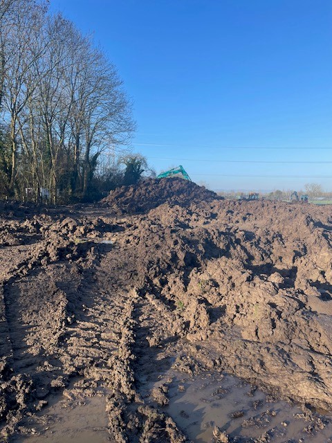 Large piles of wet clay soil with excavator in the background during bulk muck shifting and site clearance.