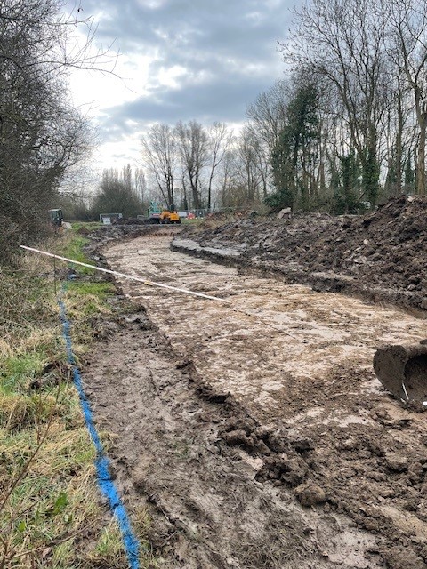 Excavated construction site with blue line marking and stripped surface, possibly for access road or drainage installation.